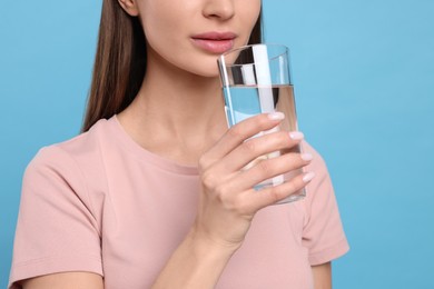 Healthy habit. Woman drinking fresh water from glass on light blue background, closeup