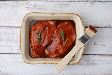 Photo of Raw marinated meat, rosemary and basting brush on white wooden table, top view