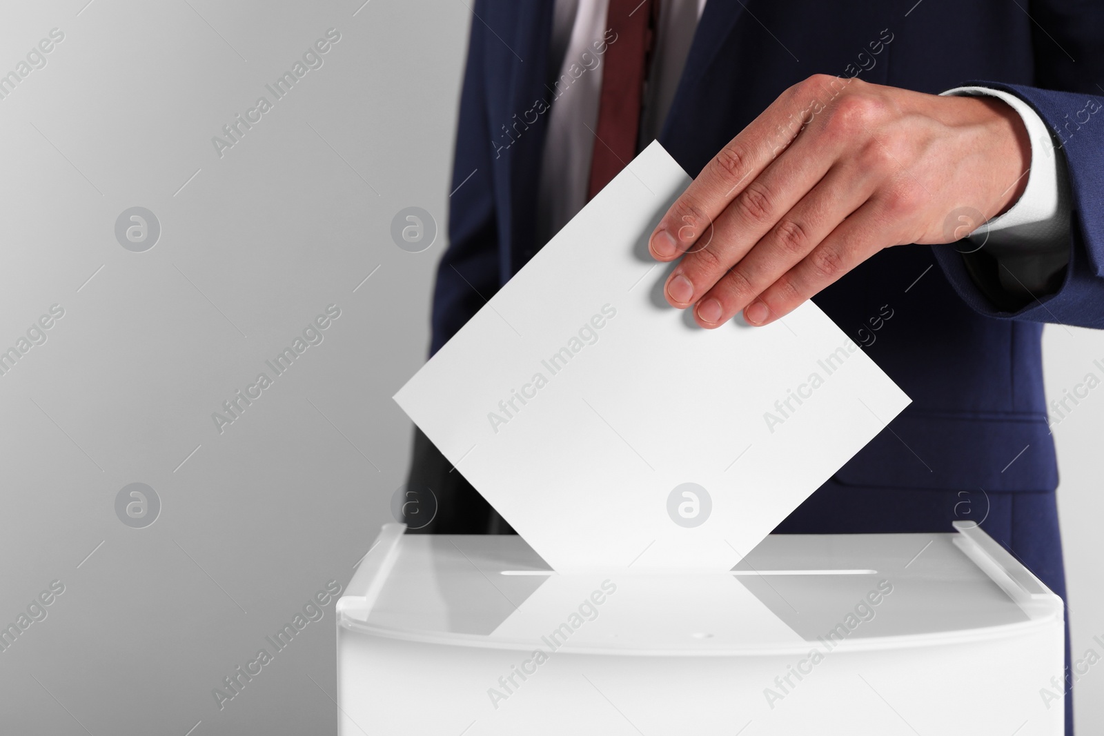 Photo of Man putting his vote into ballot box on light grey background, closeup. Space for text