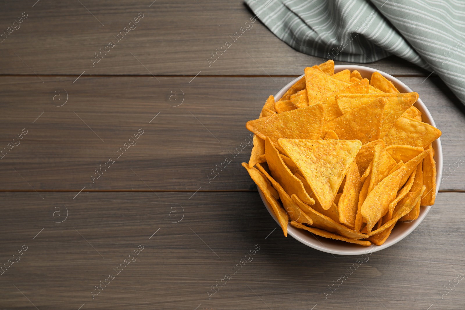Photo of Tortilla chips (nachos) in bowl on wooden table, top view. Space for text