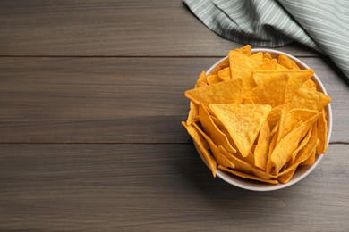 Photo of Tortilla chips (nachos) in bowl on wooden table, top view. Space for text