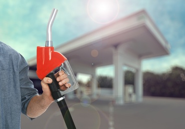 Image of Man holding fuel nozzle near gas station, closeup