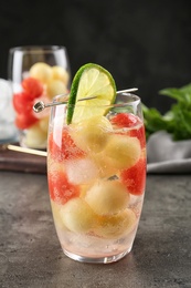 Photo of Glass of melon and watermelon ball cocktail with lime on grey table