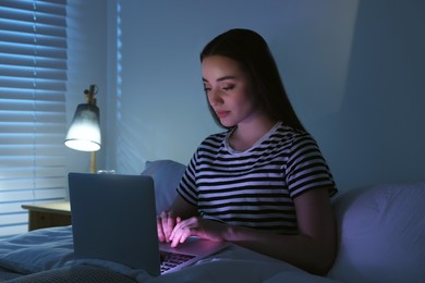 Young woman using laptop in bed at night. Internet addiction