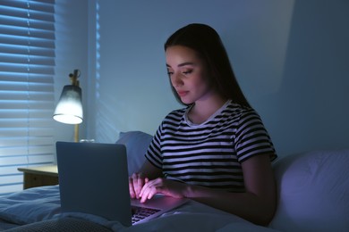 Photo of Young woman using laptop in bed at night. Internet addiction