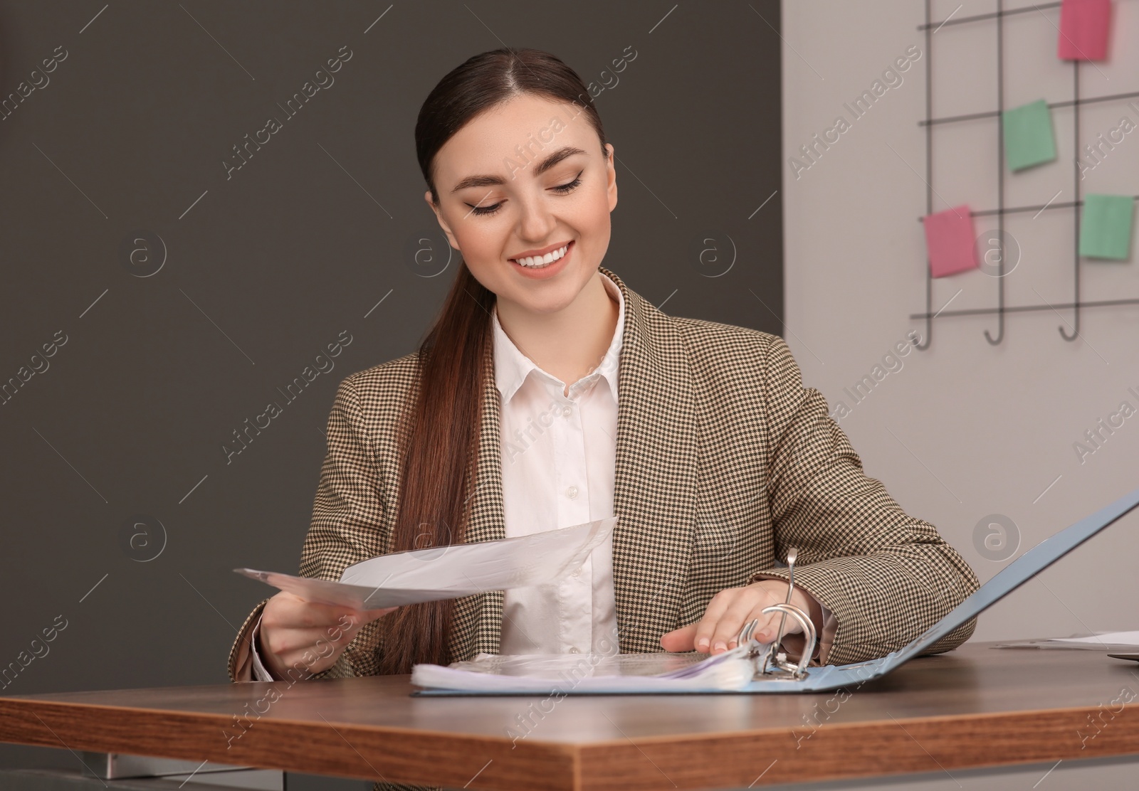 Photo of Businesswoman putting document into file folder at wooden table in office