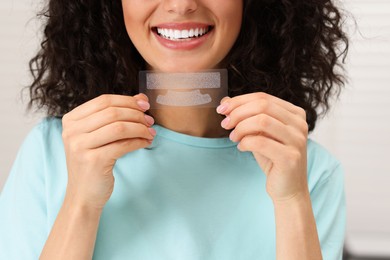 Photo of Young woman holding teeth whitening strips on light background, closeup