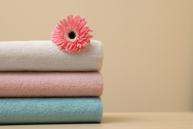 Photo of Stack of fresh towels with flower on table. Space for text