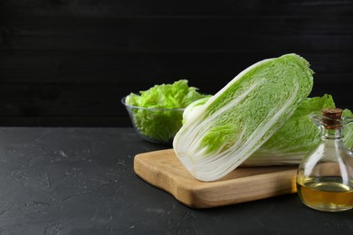 Photo of Fresh Chinese cabbages and oil on black textured table. Space for text