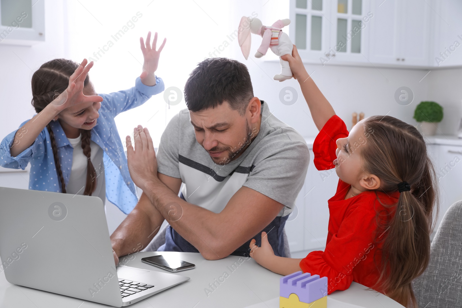 Photo of Children disturbing stressed man in kitchen. Working from home during quarantine