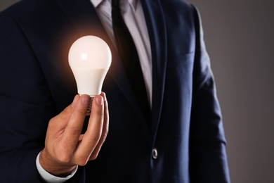 Photo of Businessman holding lamp bulb against gray background, closeup