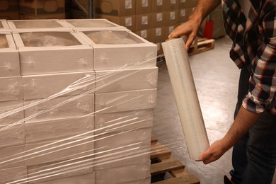 Photo of Worker wrapping boxes in stretch film at warehouse, closeup