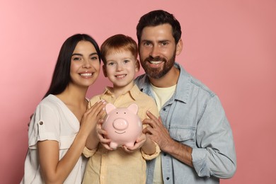 Photo of Happy family with ceramic piggy bank on pale pink background