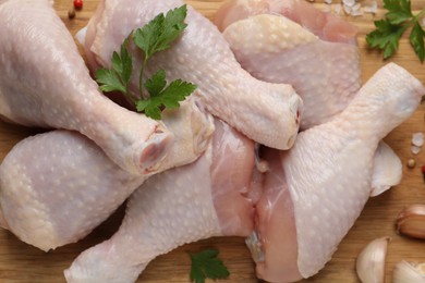 Photo of Raw chicken drumsticks with parsley, spices and garlic on wooden background, flat lay