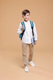Photo of Cute schoolboy with book walking on beige background