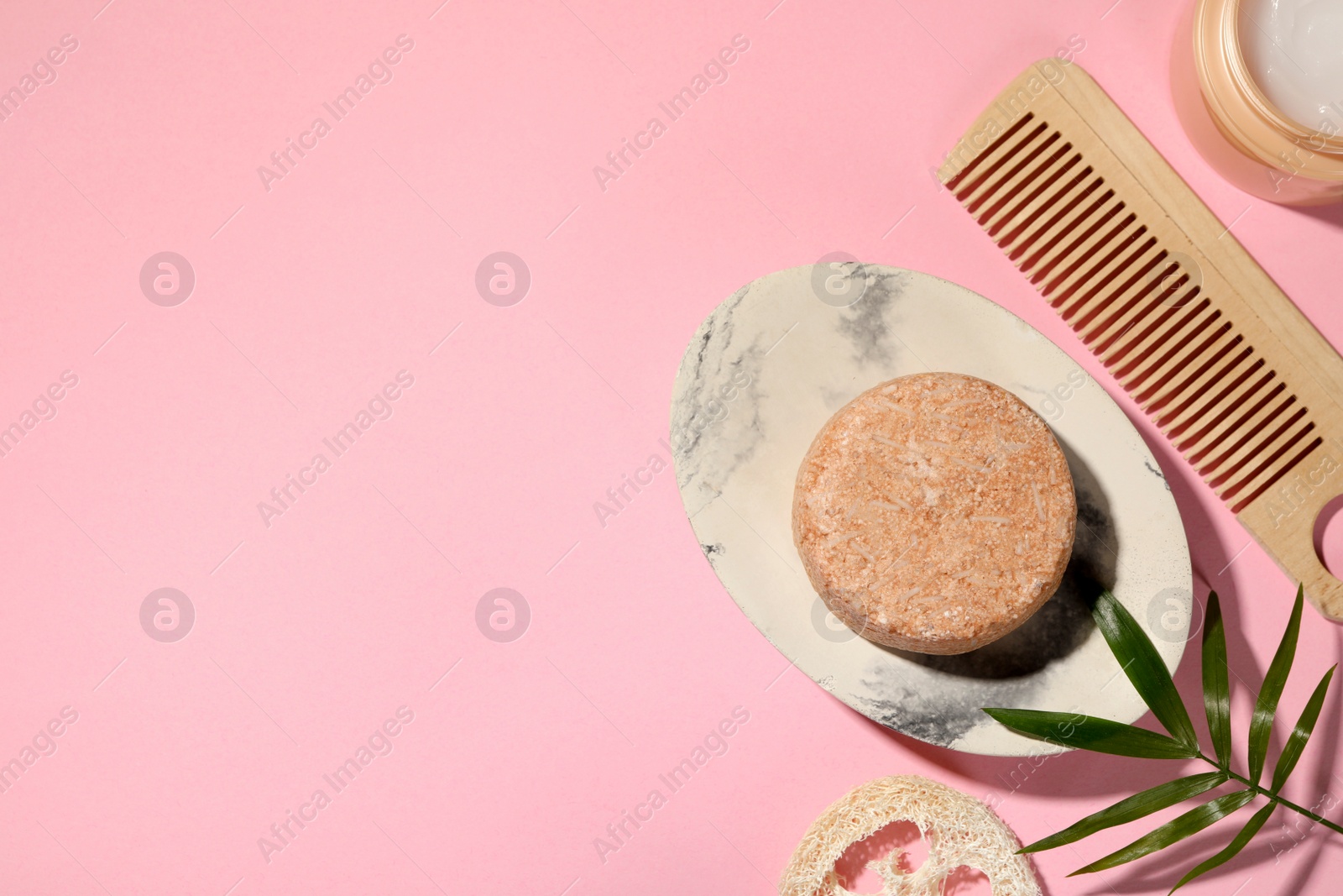 Photo of Flat lay composition of solid shampoo bar, leaf and comb on pink background. Space for text