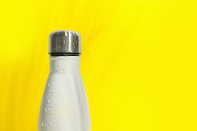 Photo of Stylish white thermo bottle with water drops on yellow background, closeup. Space for text