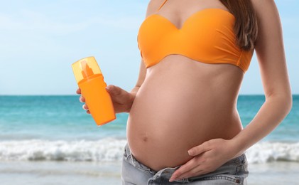 Image of Young pregnant woman with sun protection cream on beach, closeup