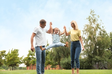 Cute little girl having fun with her parents in park on summer day