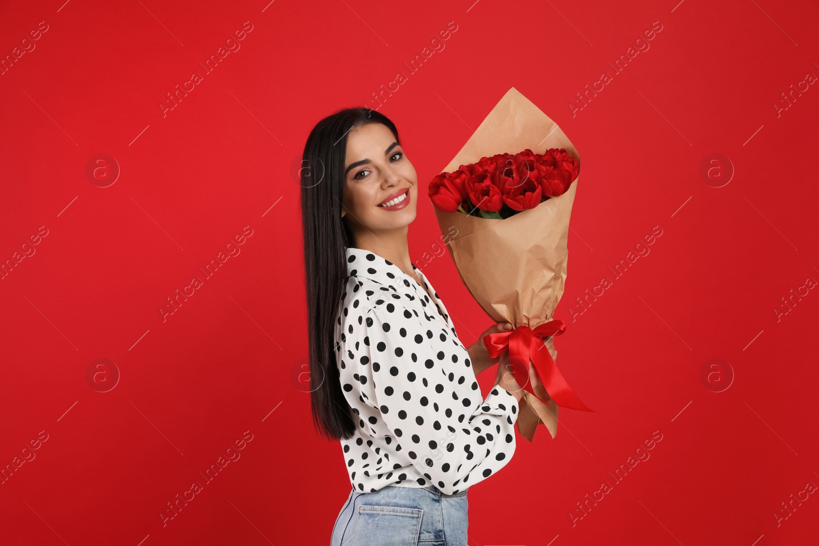 Photo of Happy woman with tulip bouquet on red background. 8th of March celebration