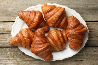 Plate with tasty croissants on wooden table, top view
