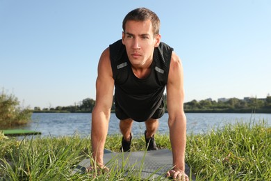 Sporty man doing straight arm plank exercise on green grass near river
