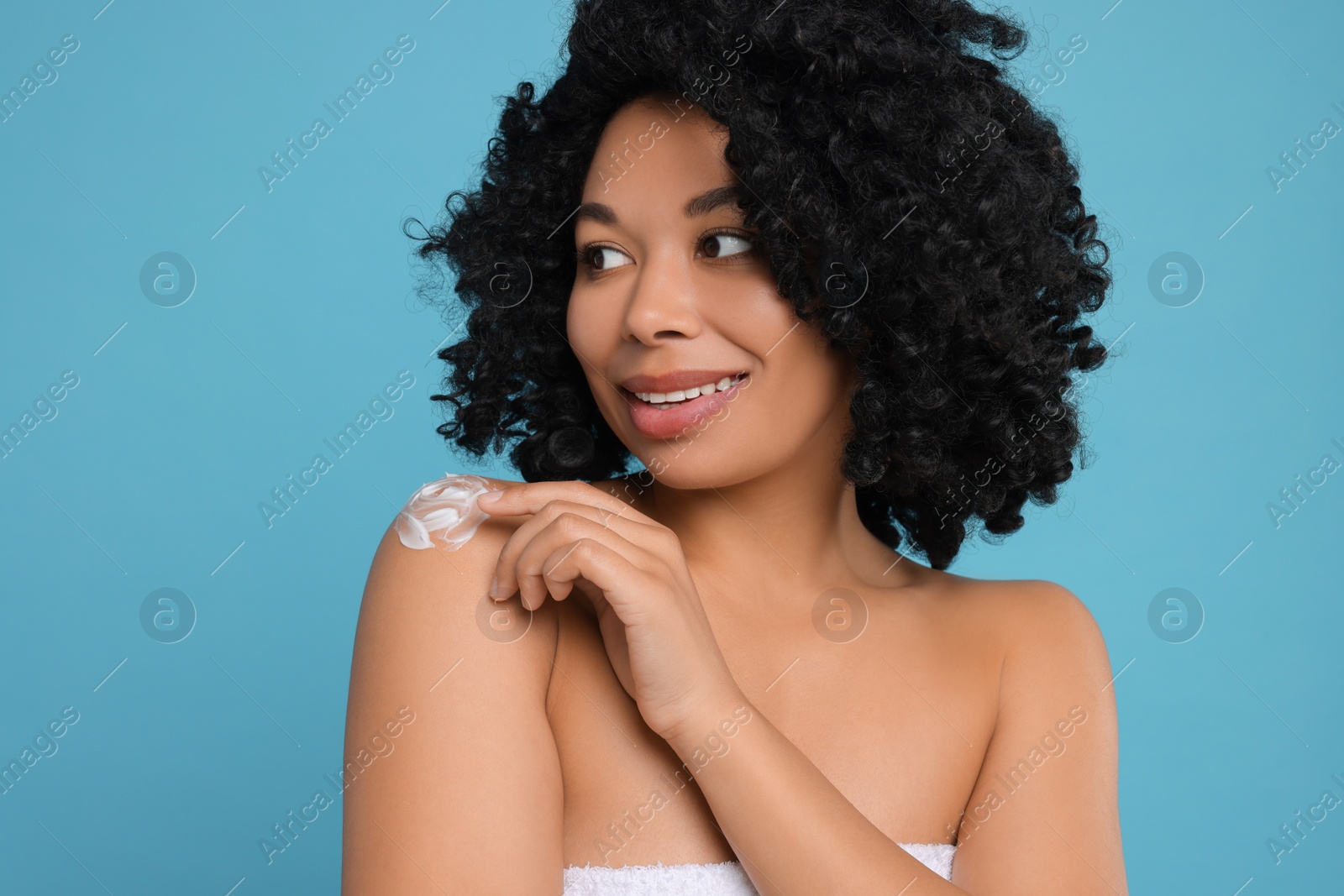 Photo of Young woman applying body cream onto shoulder on light blue background