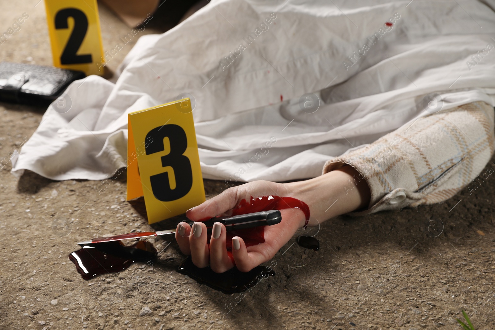 Photo of Crime scene with dead woman's body, bloody knife and markers outdoors, closeup