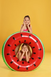 Photo of Cute little girls with bright inflatable ring on yellow background