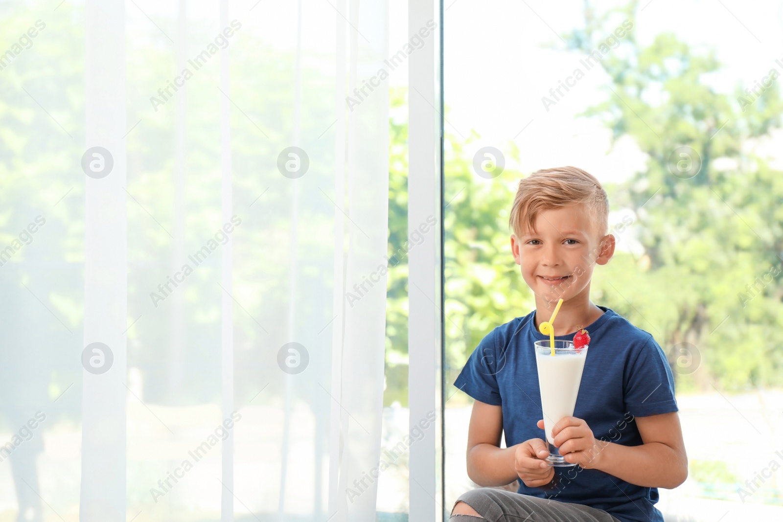 Photo of Little boy with glass of milk shake near window indoors