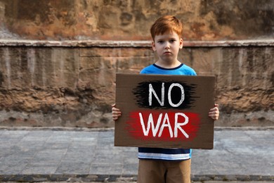 Photo of Sad boy holding poster with words No War outdoors. Space for text