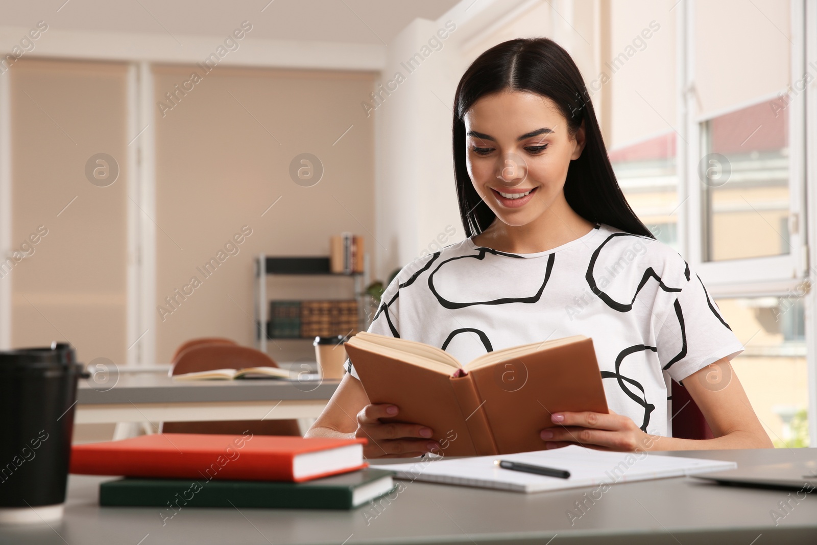 Photo of Young woman reading book at table in library