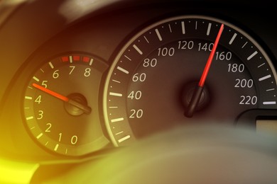 Speedometer and tachometer on car dashboard under yellow light, closeup
