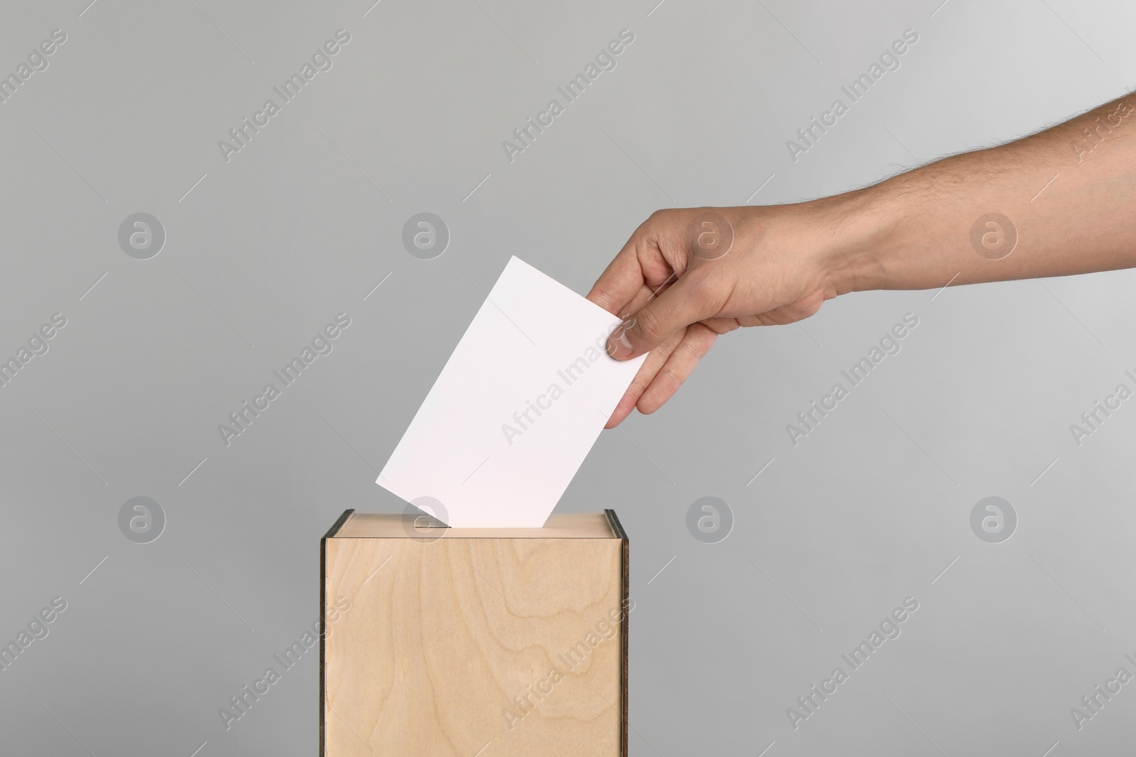 Photo of Man putting his vote into ballot box on light grey background, closeup