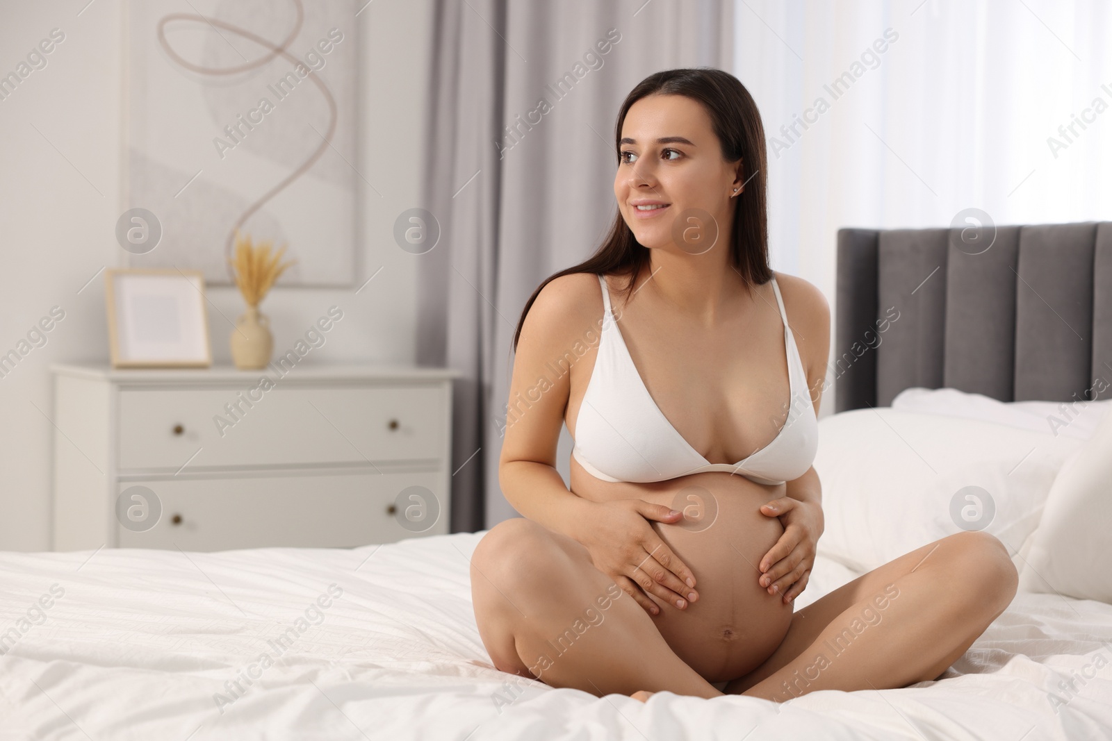 Photo of Beautiful pregnant woman in stylish comfortable underwear on bed at home, space for text