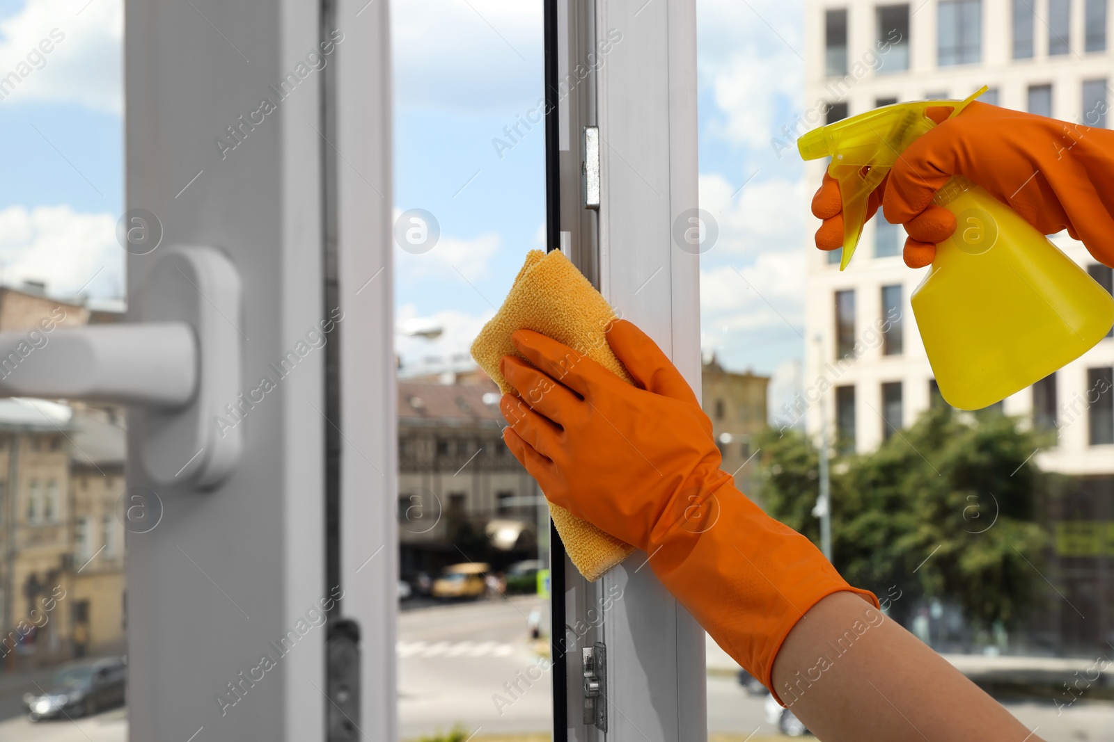 Photo of Young woman cleaning window glass with rag and detergent at home, closeup