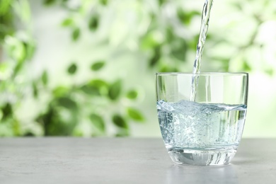 Pouring water into glass on grey table outdoors, space for text. Refreshing drink