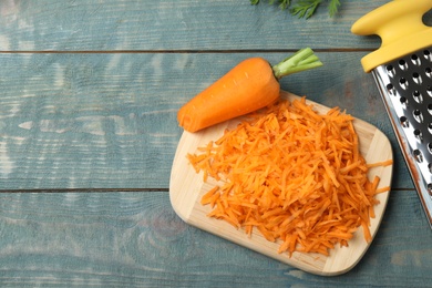 Photo of Board with grated carrot on wooden background, top view. Space for text