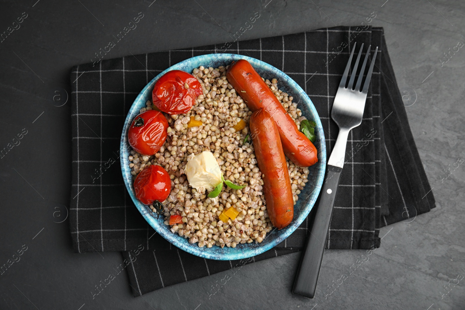 Photo of Tasty buckwheat porridge with sausages on dark grey table, flat lay