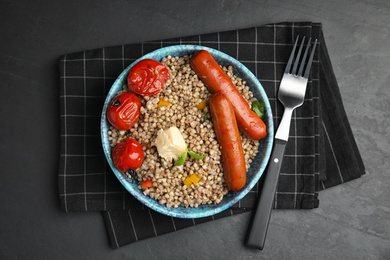 Photo of Tasty buckwheat porridge with sausages on dark grey table, flat lay