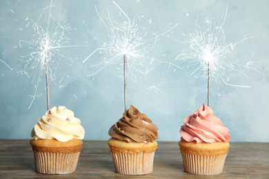 Image of Birthday cupcakes with sparklers on wooden table against light blue background