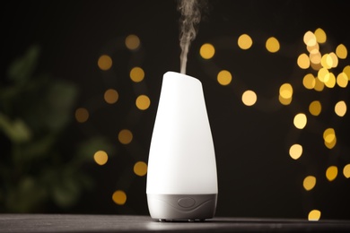 Photo of Modern aroma humidifier on wooden table against blurred lights, space for text