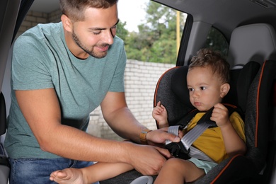 Father fastening his son with car safety belt in child seat. Family vacation