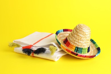 Photo of Mexican sombrero hat and poncho on yellow background