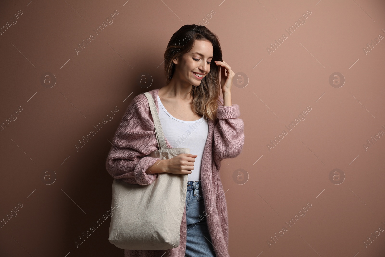 Photo of Happy young woman with blank eco friendly bag against light brown background