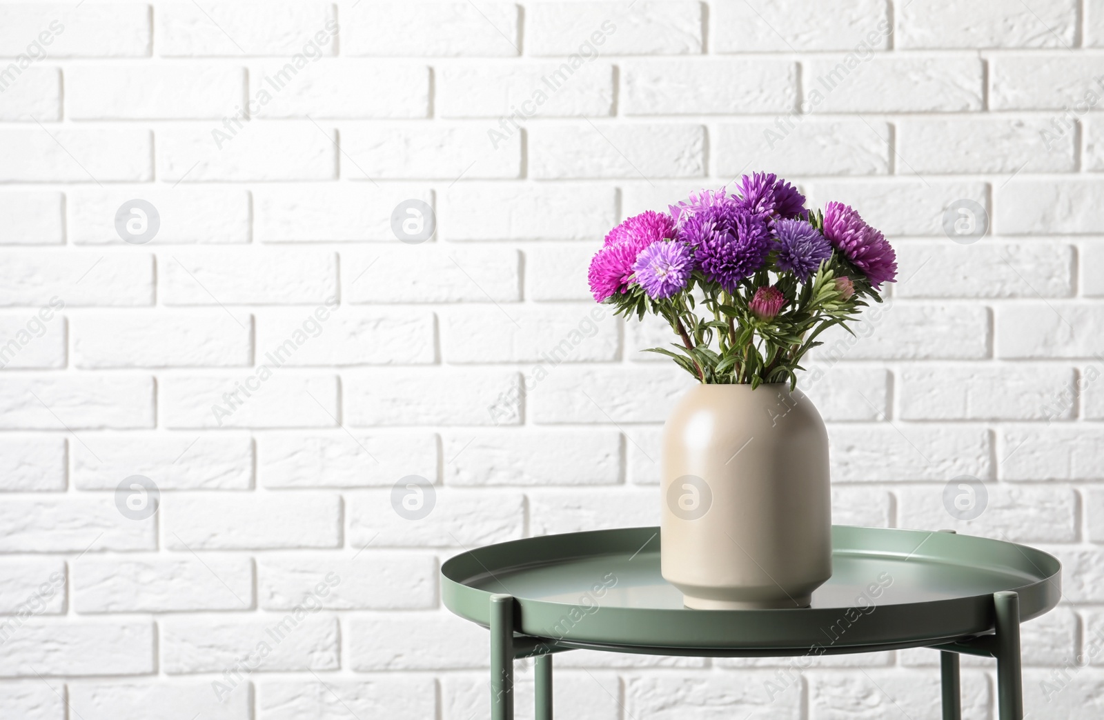 Photo of Vase with beautiful aster flower bouquet on table against brick wall. Space for text