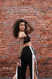 Photo of Portrait of beautiful young woman near brick wall outdoors. Hip hop dancer