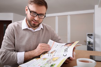 Photo of Young man reading healthy food magazine at table indoors