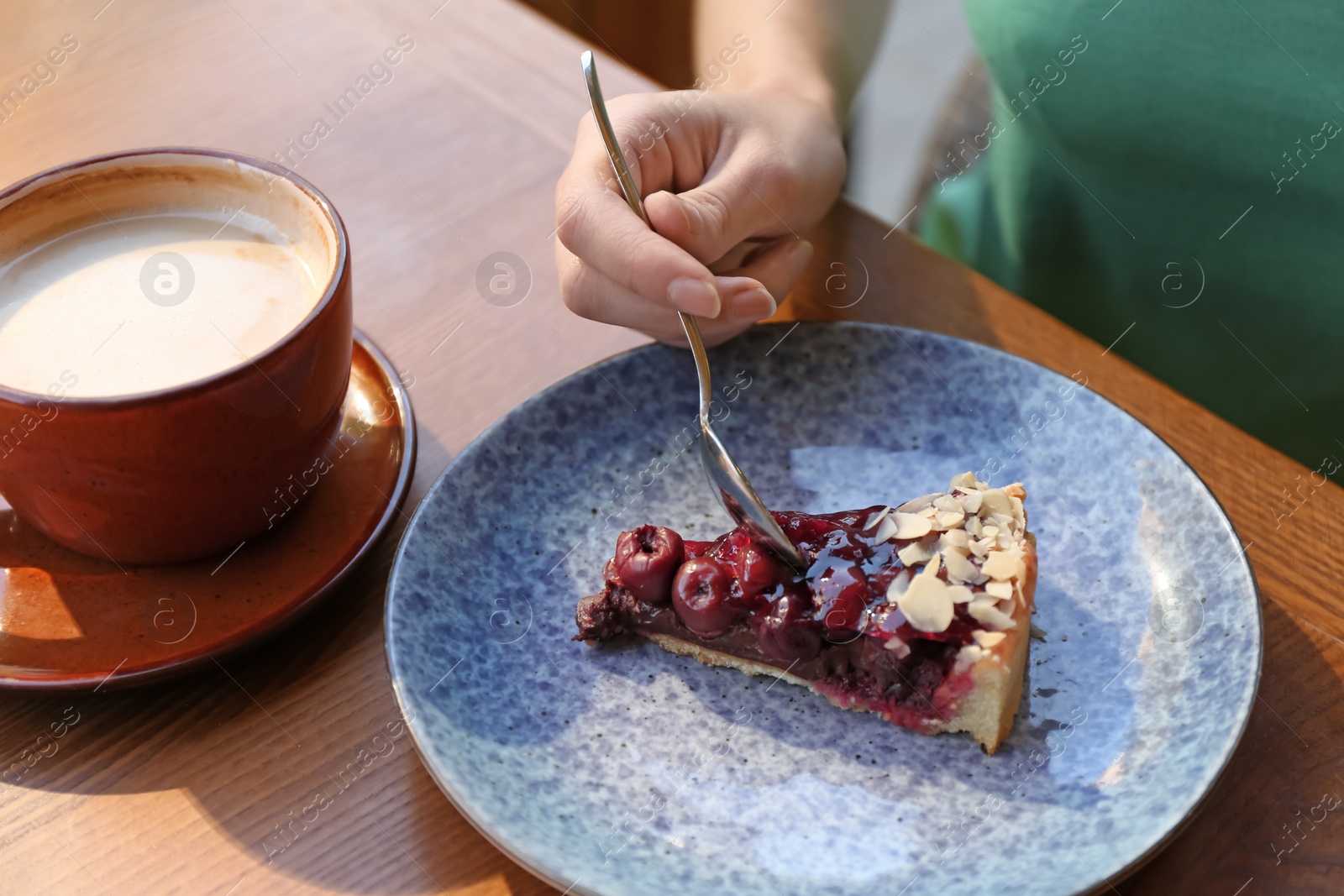 Photo of Woman eating slice of cherry cake at table, closeup