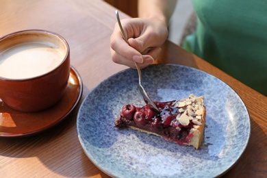 Photo of Woman eating slice of cherry cake at table, closeup